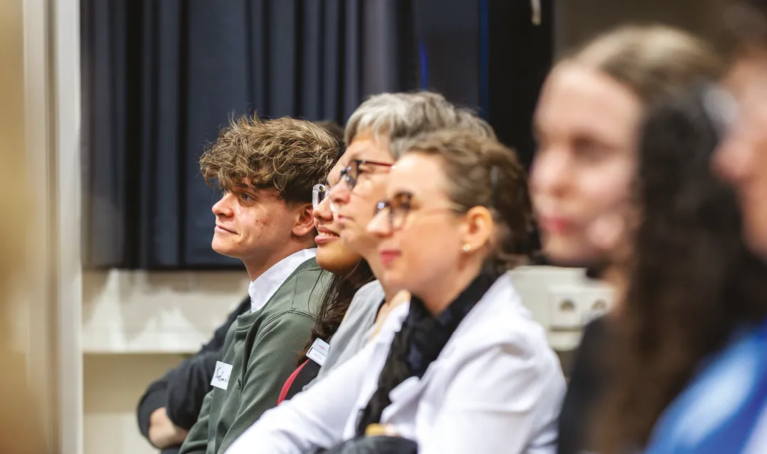 Mehrere Zuhörer:innen sitzen nebeneinander und verfolgen aufmerksam eine Präsentation oder Diskussion.