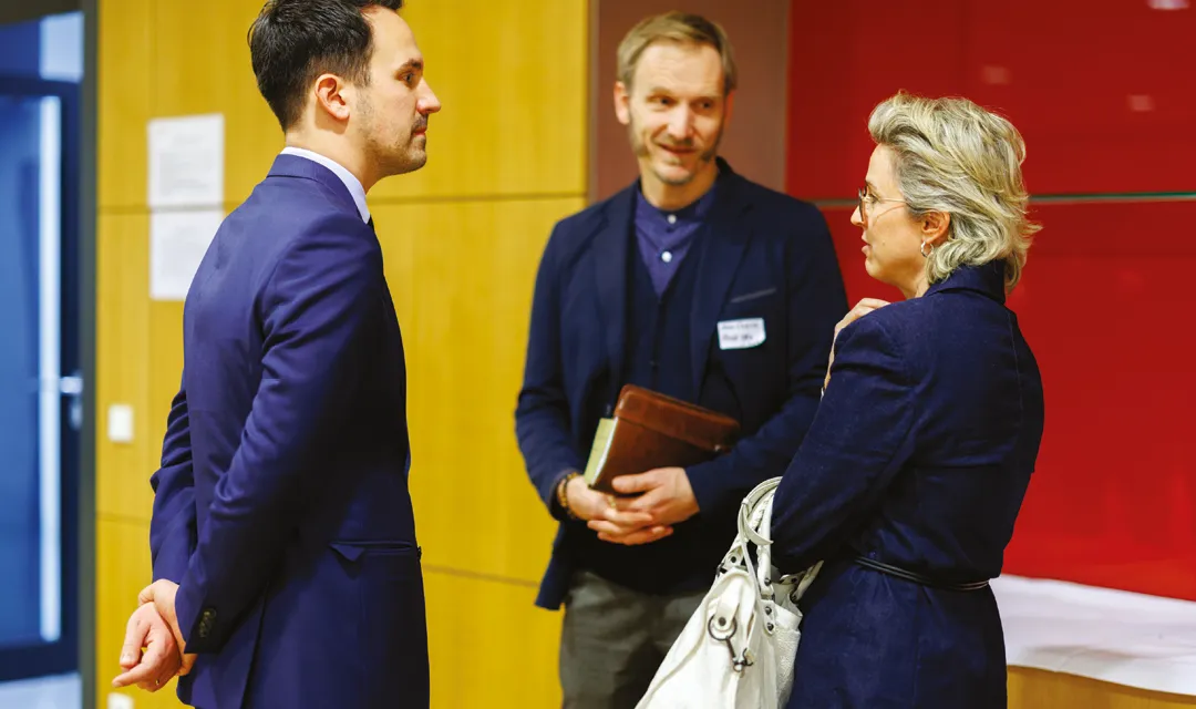 Christoph Wiederkehr spricht bei einer Veranstaltung mit zwei Personen in einem Innenraum und führt ein angeregtes Gespräch.