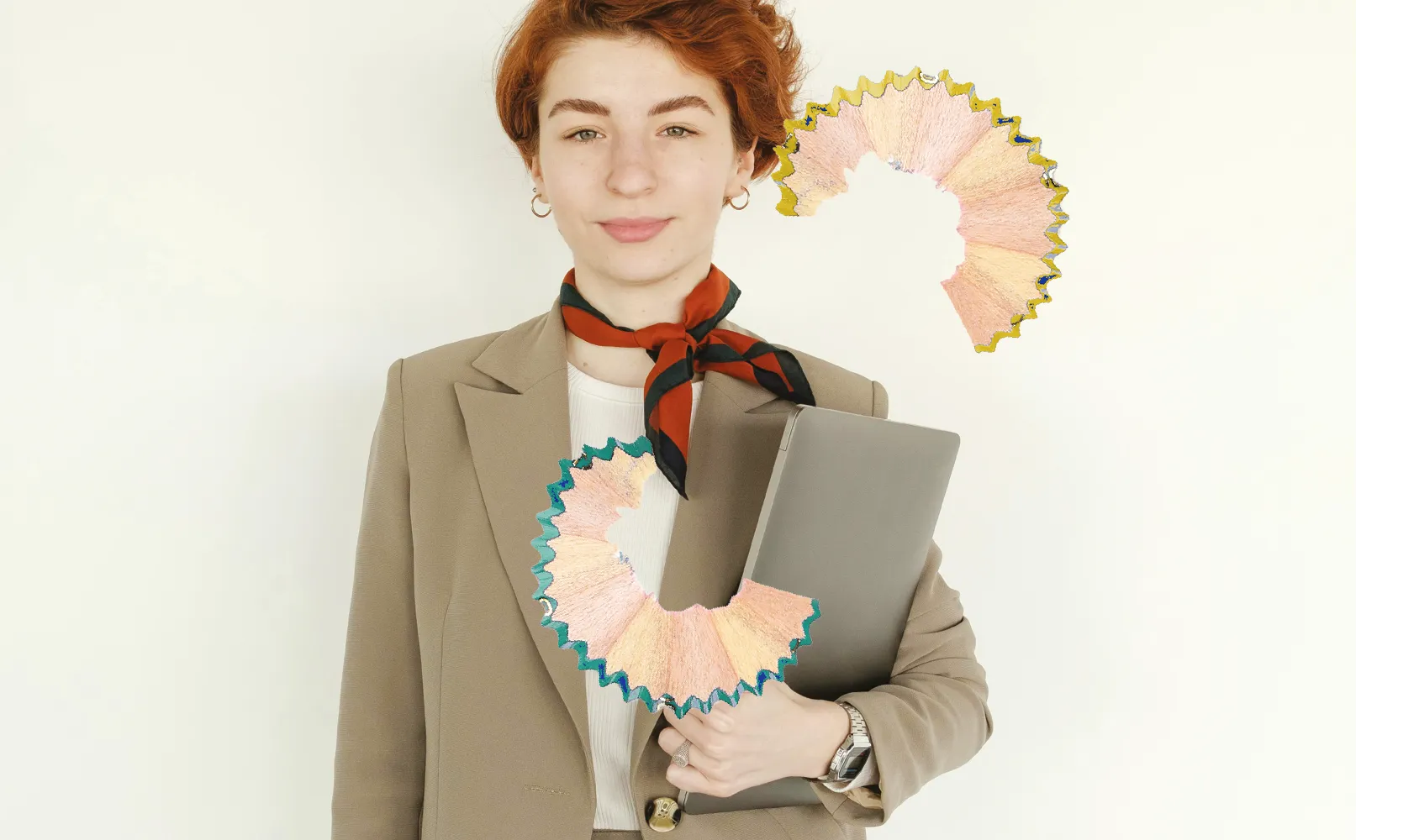 Person mit Laptop im beigen Blazer vor hellem Hintergrund, mit dekorativen Bleistiftspänen im Bild.