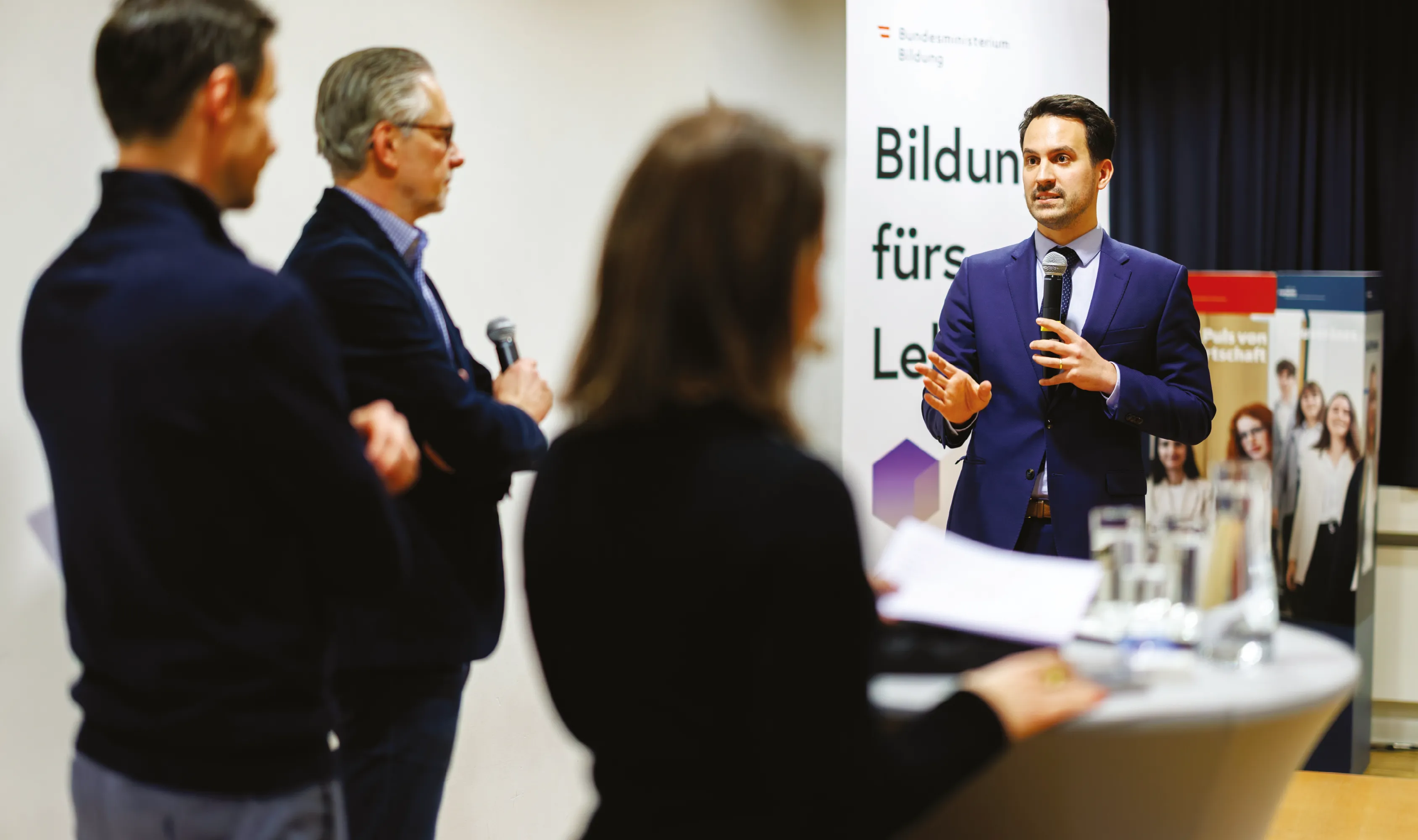 Christoph Wiederkehr spricht bei einer Veranstaltung vor einer kleinen Gruppe von Zuhörer:innen und gestikuliert mit einem Mikrofon in der Hand.